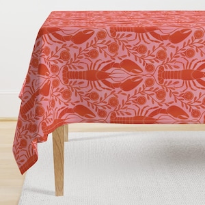 May include: A red and pink tablecloth with a repeating pattern of orange slices and lobsters. The tablecloth is draped over a wooden table.