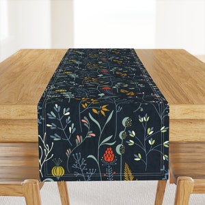 May include: A dark blue table runner with a floral pattern featuring colorful flowers and leaves. The runner has a white border.