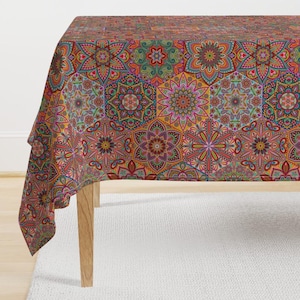 Può includere: Una tovaglia colorata con un motivo geometrico di mandala ripetuti in tonalità di rosso, arancio, giallo, verde, blu e viola. La tovaglia è drappeggiata su un tavolo di legno.