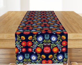 May include: A blue table runner with a colorful floral pattern. The pattern features red, yellow, orange, green, and blue flowers on a dark blue background.
