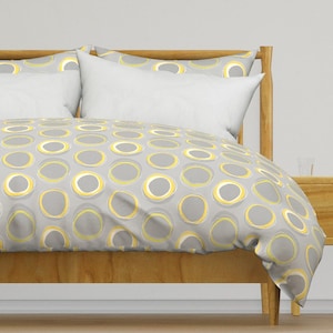 May include: A gray and yellow duvet cover with a repeating pattern of circles. The duvet cover is on a wooden bed frame.