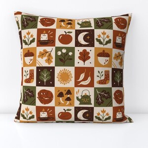 Op de afbeelding: Vierkant sierkussen met een patchwork ontwerp met herfstthema illustraties. Het ontwerp bevat eikels, bladeren, kaarsen, appels, manen en paddenstoelen in een palet van oranje, groen en bruin.