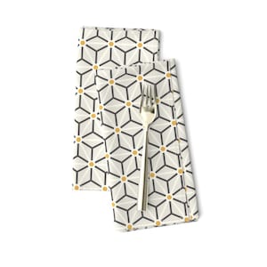 May include: Two white napkins with a geometric pattern of black lines and yellow circles. The napkins are folded and a gold fork is placed on top.