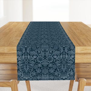 May include: A navy blue table runner with a floral pattern featuring sunflowers and grape clusters. The runner is centered on a wooden table. The floral design is in shades of blue and white.