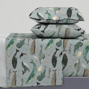 May include: A blue and white whale patterned bedding set with two matching pillowcases. The bedding features a variety of whales, including humpback whales, orcas, and narwhals.
