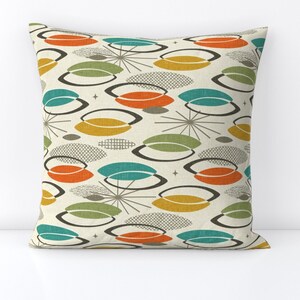 Puede incluir: Una almohada de tiro con un diseño moderno de mediados de siglo que presenta un patrón de formas abstractas de color turquesa, naranja, amarillo y verde sobre un fondo crema.