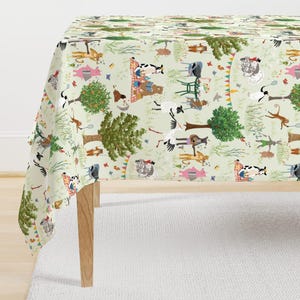May include: A light green tablecloth featuring a whimsical farm scene with various animals, trees, and picnic settings. The design includes cows, pigs, sheep, and monkeys, creating a playful and colorful pattern. The tablecloth is draped over a wooden table.