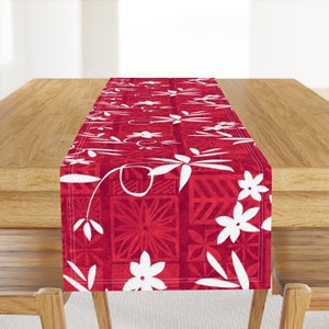 May include: Red table runner with a white floral pattern. The pattern features stylized flowers and leaves on a red background with a geometric design.