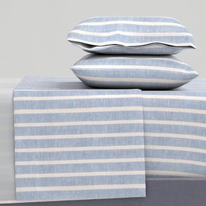 May include: A light blue and white striped bedding set. The image shows two pillowcases stacked on top of a folded sheet. The sheets and pillowcases have a classic, nautical design, with a blue and white striped pattern.