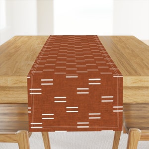 May include: A brown table runner with a white geometric pattern. The runner is on a wooden table.