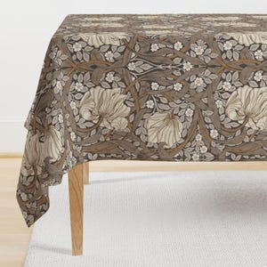 Op de afbeelding: Een bruine tafelkleed met een bloemenpatroon met witte bloemen en bladeren. Het tafelkleed is gemaakt van een zachte, geweven stof en heeft een subtiele glans.