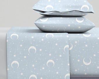 May include: A light blue bed sheet with a white crescent moon and star pattern. Two matching pillowcases are stacked on top of the sheet.
