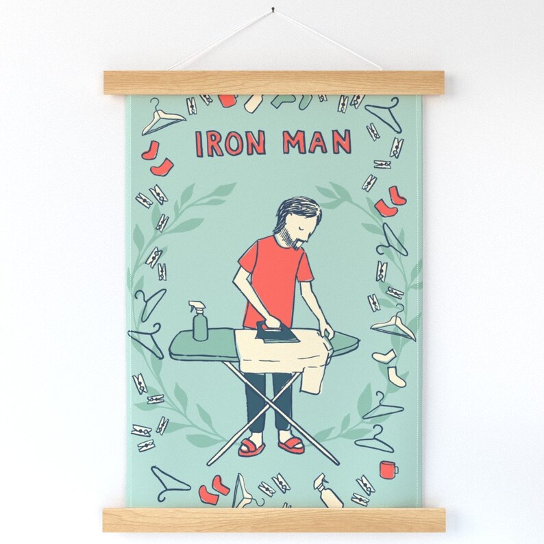 Pu&ograve; includere: Un'illustrazione blu chiaro e verde di una persona che stira con il testo "IRON MAN" in un cerchio attorno alla persona. L'illustrazione &egrave; circondata da un bordo di mollette per bucato rosse, bianche e blu.