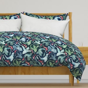 May include: A blue and green duvet cover with a repeating pattern of watercolour dragons breathing fire. The duvet cover is on a wooden bed frame.