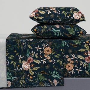 May include: A bedding set featuring two rectangular pillows stacked atop a flat sheet, all decorated with a dark navy blue background and a dense, multi-colored botanical print of various flowers, leaves, and stems in shades of peach, pink, and green.