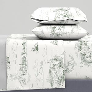 May include: White bedding set with a green toile pattern. The set includes two pillows and a folded sheet. The pattern features a detailed illustration of figures and landscapes. The overall aesthetic is classic and elegant.