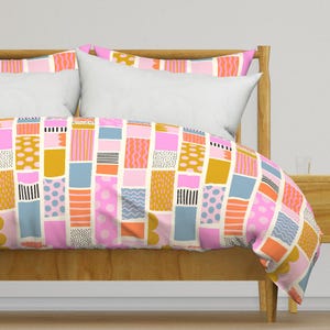 May include: A pink, blue, orange and yellow patterned duvet cover with a geometric design. The duvet cover is on a bed with a wooden headboard.