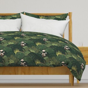 May include: A green duvet cover with a repeating pattern of stylised trees and mushrooms. The duvet cover is on a wooden bed frame.