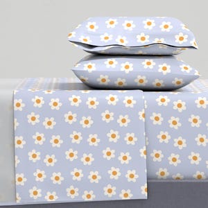 May include: A light blue bedding set featuring a daisy pattern. The set includes a fitted sheet, a flat sheet, and two pillowcases. The daisies have white petals and yellow centers. The sheets are made of a soft, comfortable material.