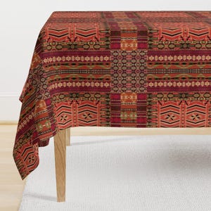 May include: A red, orange, and brown patterned tablecloth with a geometric design. The tablecloth is draped over a table with wooden legs.