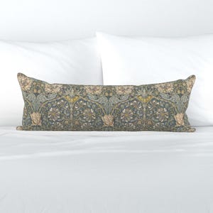 May include: A long, rectangular decorative pillow with a floral pattern in shades of blue, green, beige, and yellow. The pillow is placed on a white bed, showcasing its intricate design and color palette.