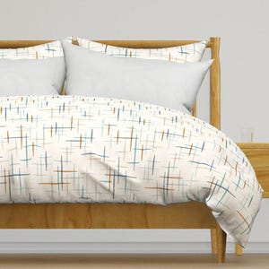 May include: White duvet cover with a geometric pattern of thin blue, brown, and beige lines on a white background. The duvet cover is on a bed with a wooden headboard.