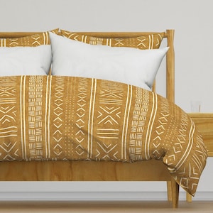 Könnte beinhalten: Ein senfgelber Bettbezug mit einem weißen geometrischen Muster. Der Bettbezug liegt auf einem Bett mit einem Holz-Kopfteil und einem weißen Kissen.