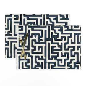 May include: Two rectangular placemats with a navy blue and off-white maze pattern. A gold fork and knife are crossed on top of one of the placemats. The placemats are made of a durable fabric.