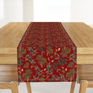 May include: Red table runner with a repeating pattern of pine branches and pine cones. The runner has a white border.