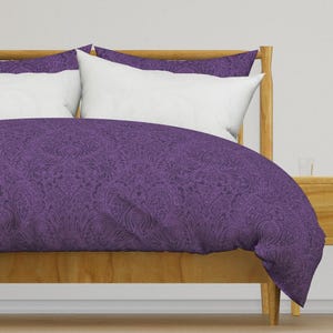 May include: A purple paisley patterned duvet cover with a white pillow on a wooden bed frame.