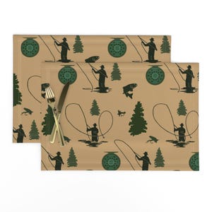 May include: A set of two brown placemats with a repeating pattern of green pine trees, silhouettes of people fly fishing, and fly fishing reels.