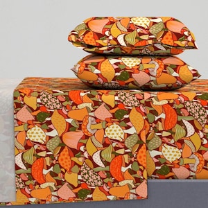 Op de afbeelding: Een set beddengoed met een paddenstoelpatroon in tinten oranje, geel, bruin en roze. De beddengoedset bevat een hoeslaken, een plat laken en twee kussenslopen.