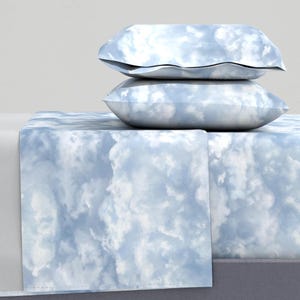 Könnte beinhalten: Ein blaues und weißes Bettuch mit Wolkenmuster und zwei passenden Kissenbezügen. Das Laken ist aus weichem, atmungsaktivem Stoff und perfekt, um Ihrem Schlafzimmer einen Hauch von Verspieltheit zu verleihen.