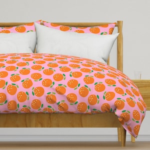 May include: Pink duvet cover with a repeating pattern of orange oranges with green leaves. The duvet cover is on a wooden bed frame.