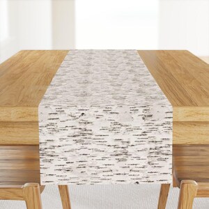 May include: A white table runner with a birch bark pattern. The runner is on a wooden table.