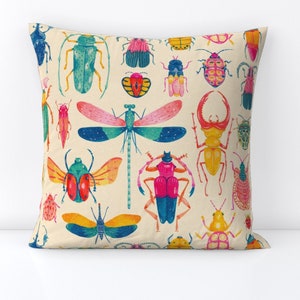 May include: A cream-colored pillow with a colorful pattern of various insects, including butterflies, beetles, and dragonflies. The insects are drawn in a whimsical style with bright colors and intricate details.