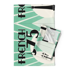 May include: A teal and white kitchen towel with a black and white graphic design. The design features the text "French 75" and a stylized image of a lamppost.