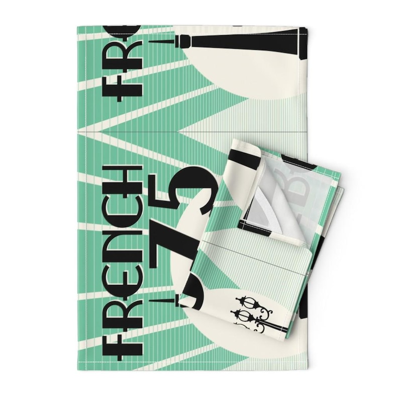 May include: A teal and white kitchen towel with a black and white graphic design. The design features the text "French 75" and a stylized image of a lamppost.