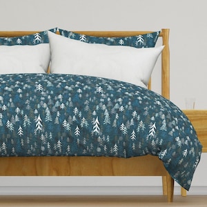 May include: A teal blue duvet cover with a white and gray forest print. The duvet cover is on a bed with a wooden headboard and a white pillow.