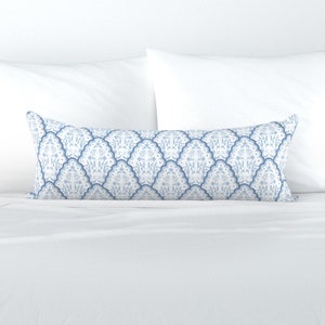 May include: A white and blue patterned lumbar pillow with a decorative design of stylised floral motifs. The pillow is on a white bed.