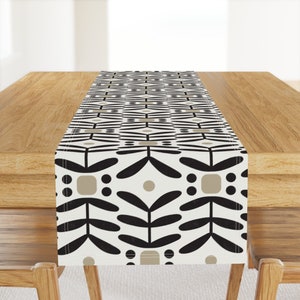 May include: A black and white geometric table runner with a beige pattern. The runner is on a wooden table.