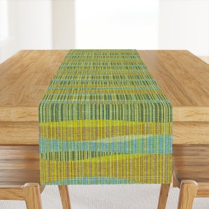 Op de afbeelding: Een groene en gele gestreepte tafelrunner met een geweven textuur. De runner ligt op een houten tafel.