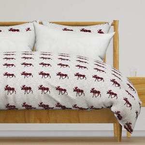 May include: A grey and white duvet cover with a red and black checked moose pattern. The duvet cover is on a wooden bed frame with two pillows.