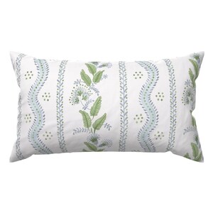 May include: A rectangular throw pillow with a white background featuring a repeating vertical pattern of green leaves, light blue wavy lines, and small green dots. The design consists of alternating botanical motifs and geometric stripes.