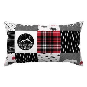 May include: A black and white patchwork pillow with a red and black plaid pattern. The pillow features a black and white mountain scene with the text "Let's sleep under the stars".