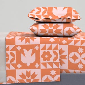 May include: A set of orange and white patterned bedding with a geometric design. The bedding includes a flat sheet, fitted sheet, and two pillowcases.