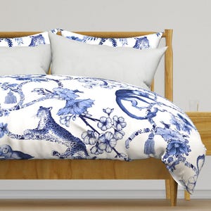 Könnte beinhalten: Weißer Bettbezug mit einem blauen und weißen Blumenmuster mit Affen, Leoparden und Quasten. Der Bettbezug befindet sich auf einem Holzbettgestell.