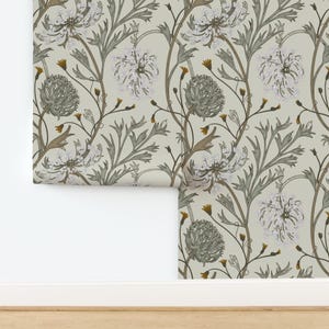 May include: Wallpaper roll with a repeating floral design. The pattern features white, spiky flowers, green leaves, and brown stems on a light beige backdrop. The wallpaper is partially unrolled, showing the pattern.