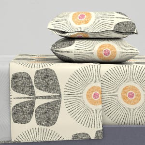 Może przedstawiać: Zestaw pościeli w kolorze białym z czarnym i pomarańczowym wzorem kwiatowym. Zestaw zawiera prześcieradło płaskie, prześcieradło z gumką i dwie poszewki na poduszki.