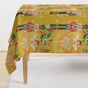 May include: A gold tablecloth with a repeating pattern of nutcracker soldiers and fairies. The nutcrackers are wearing blue and red uniforms with gold accents. The fairies are wearing white dresses with gold wings and red shoes. The background is a gold glitter pattern.